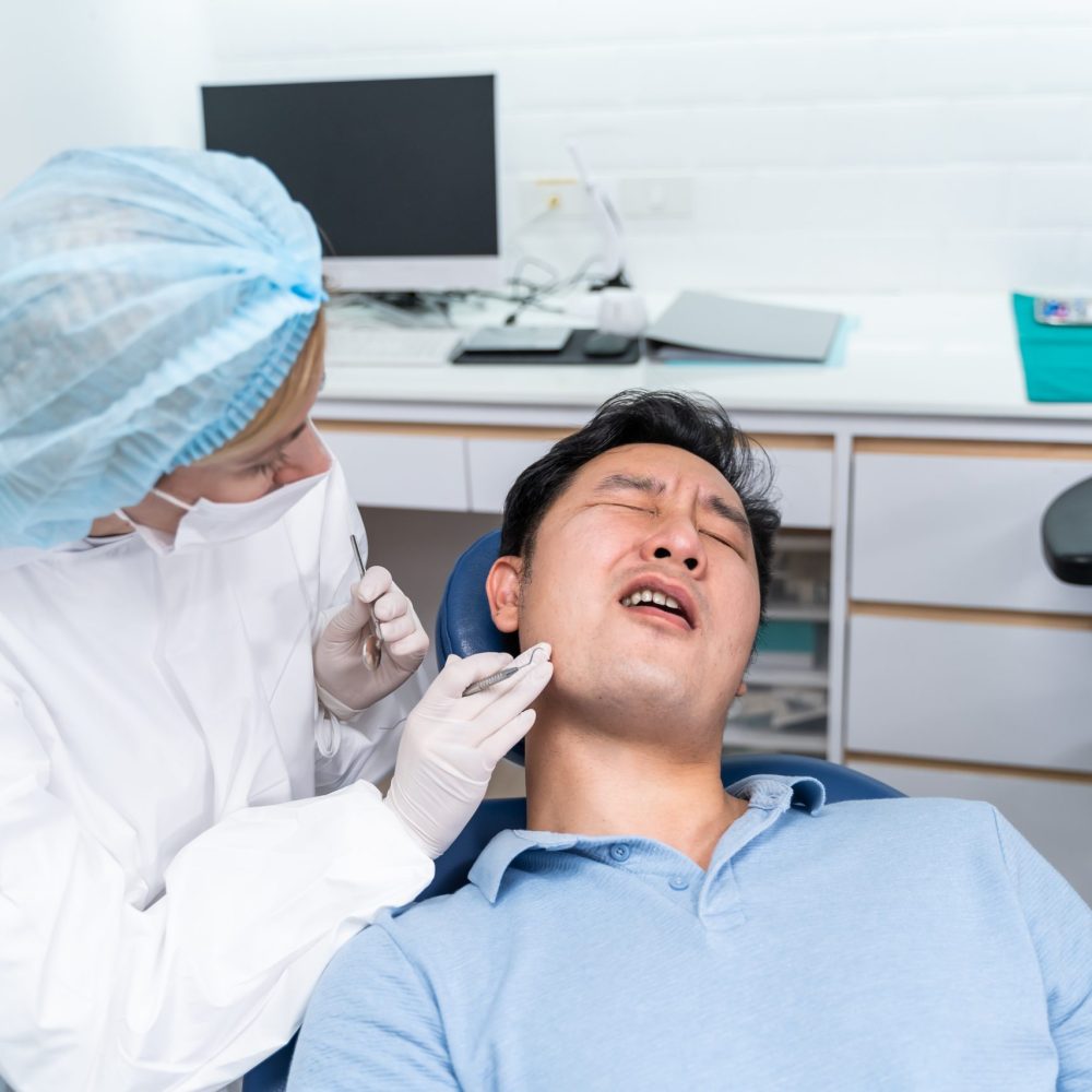Caucasian dentist examine tooth for young man patient at dental clinic. Attractive male lying on dental chair, get dental treatment from female doctor during procedure appointment service in hospital.